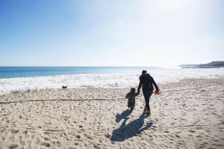 Woman play look at sea snow beach with little cute child baby boy in overalls with toy car, shovel. Mother, kid son fun on winter day. Family holiday 15 may love parents children concept. Back viewの写真素材
