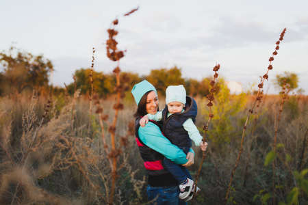 Tender woman in turquoise hat standing at dry high grass background hugging little cute child baby boy on nature. Mother, little kid son. Parenthood family day 15 of may love parents children conceptの写真素材
