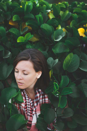 Portrait of young attractive beautiful cutie brunette woman standing in summer warm sunny day in green bushes with big leaves in front of stone rock fence. Sensualityの写真素材