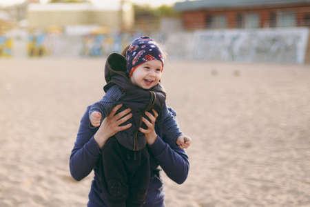 Young woman playing at sea sand beach background with little cute child baby boy, good mood. Mother, little kid son on sunny day. Parenthood, family holiday 15 of may, love, parents, children conceptの写真素材
