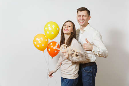 Cute couple in love. Man, woman with wooden word Love, yellow, orange balloons isolated on white background. For advertisement. St. Valentine's Day, International Women's Day birthday holiday conceptの写真素材