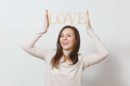 Beautiful young smiling woman in light casual clothes holding above her head wooden word love on white background. Copy space for advertisement. St Valentines Day or International Women's Day conceptの写真素材