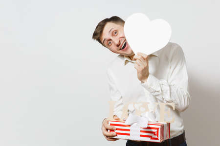 Young fun handsome smiling man holding big white heart, wooden word Love, present box with gift isolated on white background. St. Valentine's Day, International Women's Day, birthday, holiday conceptの写真素材