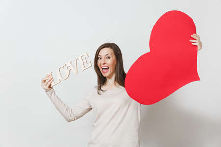 Effective young smiling woman holding big red heart, wooden word love on white background. Copy space for advertisement. With place for text. St. Valentine's Day or International Women's Day conceptの写真素材