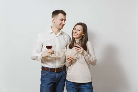 Young caucasian couple. Happy smiling man and woman in love in casual light clothes, jeans making toast, drinking from glasses of red wine isolated on white background. Copy space for advertisementの写真素材