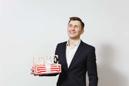 Young man in suit holding wooden word Love, red present box with gift isolated on white background. Copy space for advertisement. St. Valentines Day, International Womens Day birthday holiday conceptの写真素材