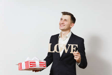 Young man in suit holding wooden word Love, red present box with gift isolated on white background. Copy space for advertisement. St. Valentines Day, International Womens Day birthday holiday conceptの写真素材