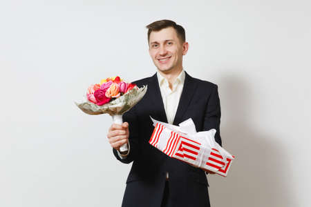 Young handsome man in suit holding bouquet of beautiful roses flowers, red present box with gift isolated on white background. St. Valentine's Day, International Women's Day birthday holiday conceptの写真素材