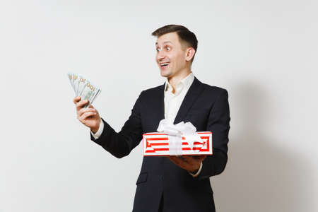 Young handsome man in suit holding red present box with gift, bundle of cash money dollars isolated on white background. St. Valentine's Day, International Women's Day, birthday holiday conceptの写真素材