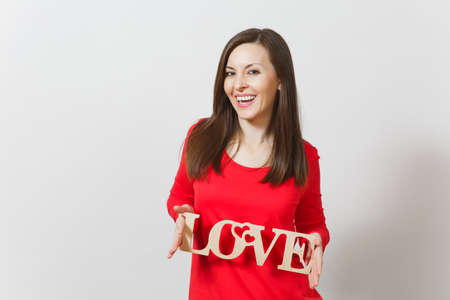Beautiful young brunette fun smiling woman in red casual clothes holding wooden word love on white background. Copy space for advertisement. St. Valentine's Day or International Women's Day conceptの写真素材