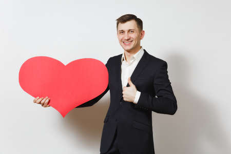 Young man in suit showing thumb up holding big red heart isolated on white background. Copy space, advertisement. Place for text. St. Valentine's Day, International Women Day birthday holiday conceptの写真素材