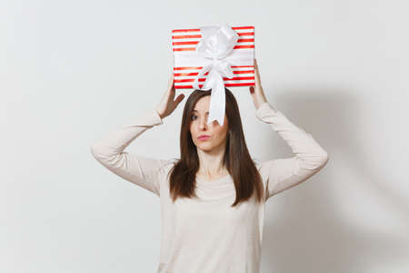 Fun woman holding above her head red striped present box with ribbon isolated on white background. For advertisement. St. Valentines Day, International Womens Day, Christmas birthday, holiday conceptの写真素材