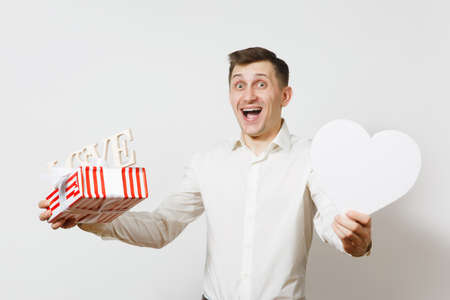Young fun handsome smiling man holding big white heart, wooden word Love, present box with gift isolated on white background. St. Valentine's Day, International Women's Day, birthday, holiday conceptの写真素材