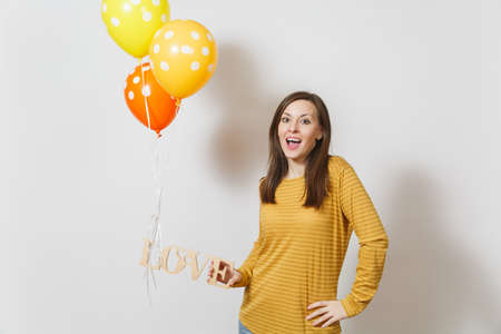 Beautiful romantic young smiling woman holding wooden word love, yellow orange air balloons on white background. Copy space for advertisement. St. Valentine's Day or International Women's Day conceptの写真素材
