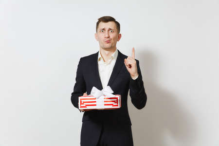Man in suit pointing index finger up holding red present box with gift isolated on white background. Copy space for advertisement. St. Valentines Day International Womens Day birthday holiday conceptの写真素材