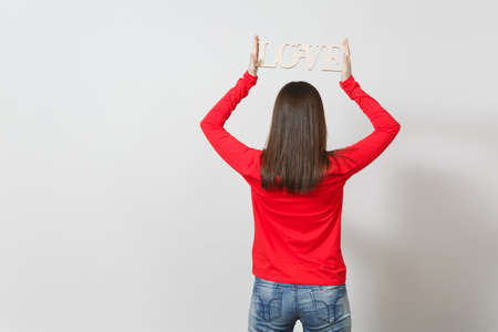 Young woman in red casual clothes turning back to camera, holding wooden word love above head on...