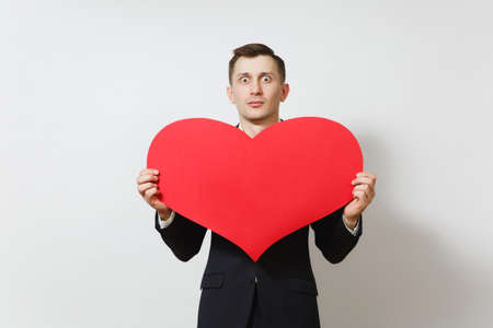 Young stunned shocked upset sad man in suit holding big red heart isolated on white background. Copy space for advertisement. St. Valentine's Day, International Women's Day, birthday, holiday conceptの写真素材