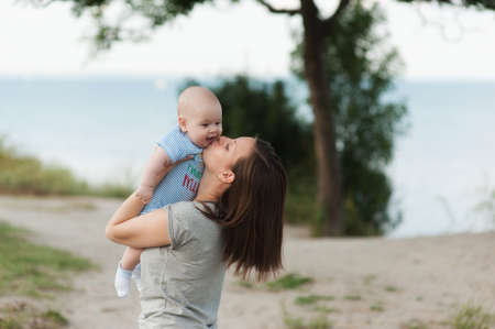 Young fun smiling woman standing at sea background hugging little cute child baby boy on nature, green trees. Mother, little kid son. Parenthood, family day 15 of may, love, parents, children conceptの写真素材