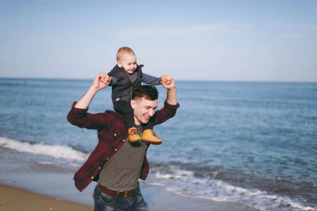 Man playing at sea sand beach background with little cute child baby boy, good mood. Father keeps on shoulders little kid son. Parenthood, family holiday day15 of may, love, parents, children conceptの写真素材