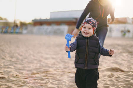 Young woman playing at sea sand beach background with little cute child baby boy, good mood. Mother, little kid son on sunny day. Parenthood, family holiday 15 of may, love, parents, children conceptの写真素材