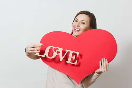 Effective young smiling woman holding big red heart, wooden word love on white background. Copy space for advertisement. With place for text. St. Valentine's Day or International Women's Day conceptの写真素材