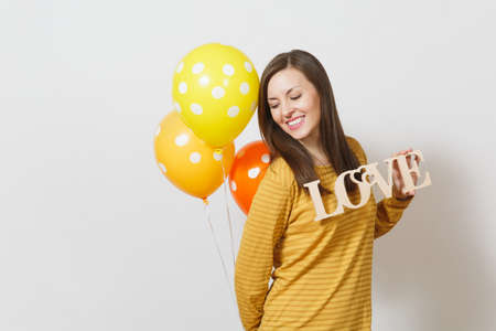 Beautiful romantic young smiling woman holding wooden word love, yellow orange air balloons on white background. Copy space for advertisement. St. Valentine's Day or International Women's Day conceptの写真素材