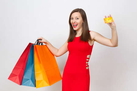 Attractive glamour fashionable young brown-hair woman in red dress holding credit card, multi colored packets with purchases after shopping isolated on white background. Copy space for advertisementの写真素材