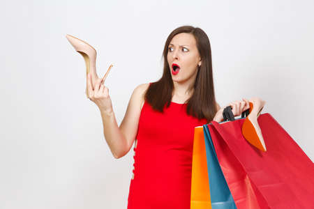 Attractive impressive glamour caucasian fashionable young brown-hair woman in red dress holding beige shoes with red sole, multi colored packets with purchases, shopping isolated on white backgroundの写真素材