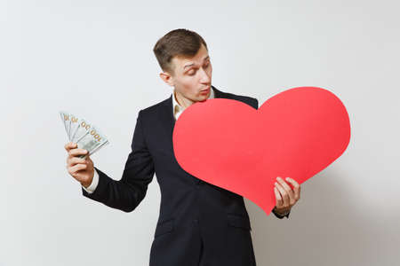 Young man in suit with big red heart, bundle of cash money dollars isolated on white background. Copy space for advertisement. St. Valentine's Day, International Women's Day, birthday holiday conceptの写真素材