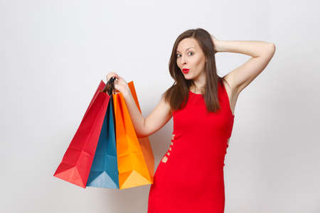 Attractive glamour caucasian fashionable young brown-hair woman in red dress holding multi colored packets with purchases after shopping isolated on white background. Copy space for advertisementの写真素材