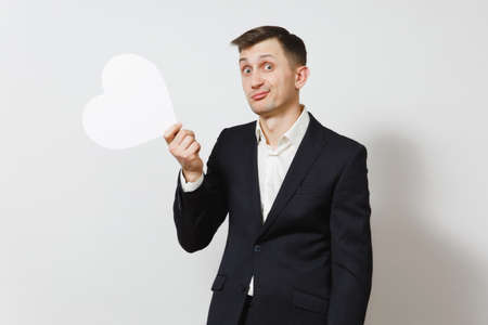 Young stunned shocked upset sad man in suit holding big white heart isolated on white background. Copy space for advertisement. St. Valentine's Day, International Women's Day birthday holiday conceptの写真素材
