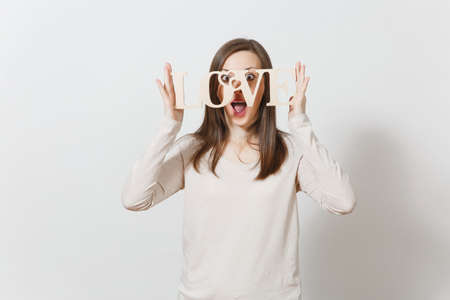 Beautiful young fun smiling woman in light casual clothes hiding behind wooden word love on white background. Copy space for advertisement. St. Valentine's Day or International Women's Day conceptの写真素材