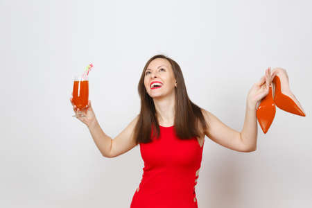 Beautiful glamour fashionable young brown-hair woman in red dress holding glass of drink cocktail, beige shoes with red sole of her shopping isolated on white background. Copy space for advertisementの写真素材
