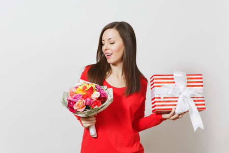 Young pretty woman in red clothes holding bouquet of beautiful roses flowers, present box with gift isolated on white background. St Valentines Day, International Women's Day birthday holiday conceptの写真素材