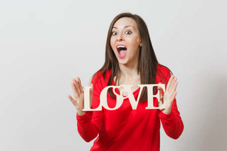 Beautiful young brunette fun smiling woman in red casual clothes holding wooden word love on white background. Copy space for advertisement. St. Valentine's Day or International Women's Day conceptの写真素材
