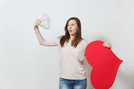 Sad upset lamentable woman holding big red heart, bundle of cash money dollars on white background. Copy space for advertisement. Place for text. St Valentine's Day, International Women's Day conceptの写真素材