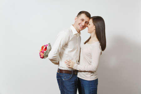 Couple in love. Woman looking behind man who hiding behind him bouquet of beautiful roses flowers isolated on white background. St. Valentine's Day, International Women's Day birthday holiday conceptの写真素材
