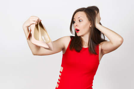 Attractive glamour caucasian fashionable young pensive perplexed brown-hair woman in red dress getting beige shoes with red sole of shopping isolated on white background. Copy space for advertisementの写真素材