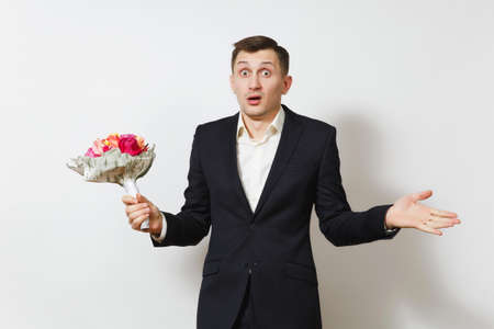 Young handsome perplexed man in suit spreading hands, holding bouquet of beautiful roses flowers isolated on white background. St. Valentine's Day, International Women's Day, birthday holiday conceptの写真素材
