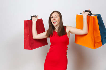 Attractive glamour caucasian fashionable young brown-hair woman in red dress holding multi colored packets with purchases after shopping isolated on white background. Copy space for advertisementの写真素材