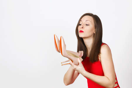 Attractive glamour caucasian fashionable young pensive perplexed brown-hair woman in red dress getting beige shoes with red sole of shopping isolated on white background. Copy space for advertisementの写真素材
