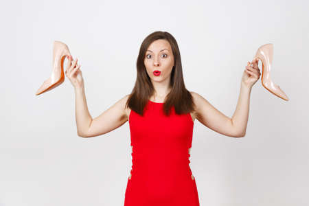 Attractive glamour caucasian fashionable young smiling brown-hair woman in red dress holding beige shoes with red sole of her shopping isolated on white background. Copy space for advertisementの写真素材