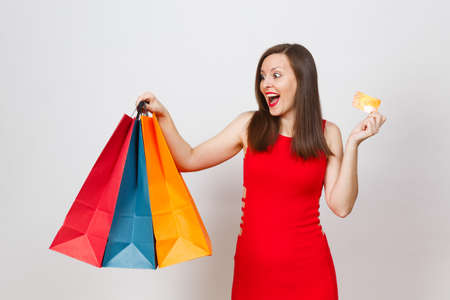 Attractive glamour fashionable young brown-hair woman in red dress holding credit card, multi colored packets with purchases after shopping isolated on white background. Copy space for advertisementの写真素材
