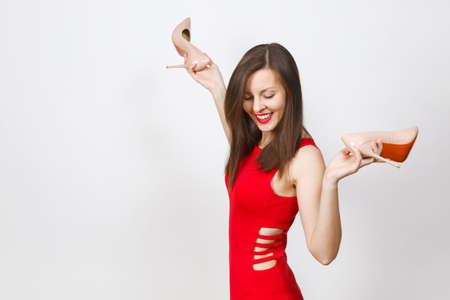 Attractive glamour happy caucasian fashionable young smiling brown-hair woman in red dress getting beige shoes with red sole of her shopping isolated on white background. Copy space for advertisementの写真素材
