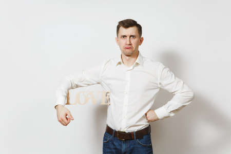 Young confused sad upset man in shirt holding wooden word Love isolated on white background. Copy space for advertisement. St. Valentine's Day, International Women's Day, birthday, holiday conceptの写真素材