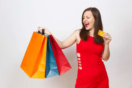 Pretty impressive fashionable young brown-hair woman in red dress holding credit card, multi colored packets with purchases after shopping isolated on white background. Copy space for advertisementの写真素材