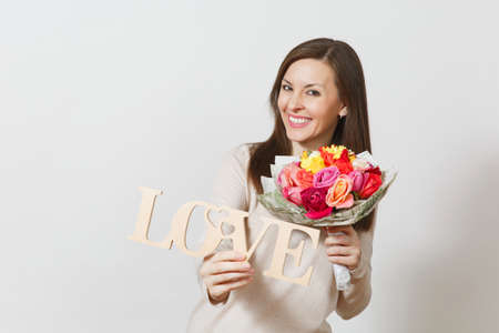 Young smiling woman holding wooden word Love, bouquet of beautiful roses flowers isolated on white background. Copy space for advertisement. St. Valentine's Day or International Women's Day conceptの写真素材