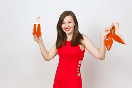 Beautiful glamour fashionable young brown-hair woman in red dress holding glass of drink cocktail, beige shoes with red sole of her shopping isolated on white background. Copy space for advertisementの写真素材