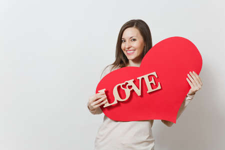 Effective young smiling woman holding big red heart, wooden word love on white background. Copy space for advertisement. With place for text. St. Valentine's Day or International Women's Day conceptの写真素材