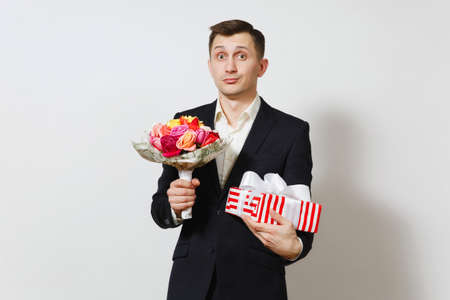 Young handsome man in suit holding bouquet of beautiful roses flowers, red present box with gift isolated on white background. St. Valentine's Day, International Women's Day birthday holiday conceptの写真素材
